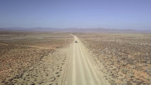 Aerial of SUV traveling along a dusty dirt road in semi-arid desert.
