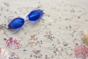 Enjoying vacation mood, swimming glasses on white sand background. Space for a text or product display, top view.