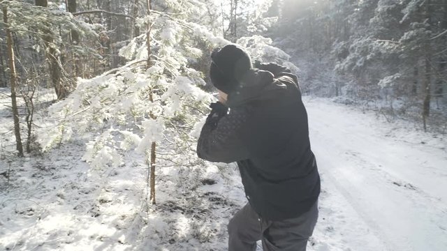 A young man is photographing a fur-tree in a winter forest.