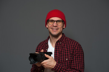 Portrait of positive young male photographer holding camera against a gray background