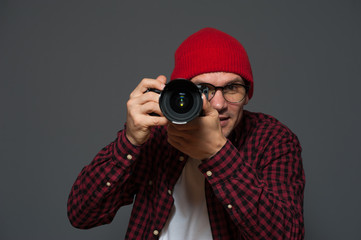 Positive blurred hipster man in stylish clothes photographer holds camera and takes photo on background in violet color tone