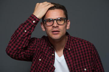 Obraz premium Portrait of worried man with glasses and in casual clothes holding his hand on head depicting an alarm or dandruff on gray background