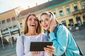 Two young beautiful happy women  smiling ,talking and looking something on digital tablet.