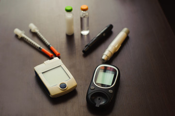 medicine, diabetes and health care concept - close up of blood sugar test stripe, glucometer, insulin pen and other diabetic tools on table