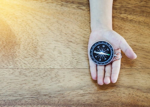 Kid Hands Holding Compass On Wooden Table. Copy Space