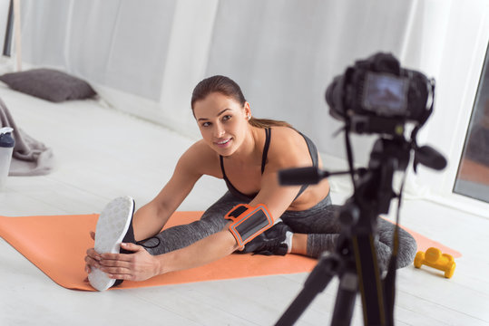 Being healthy. Attractive alert muscular dark-haired young blogger smiling and stretching while sitting on the carpet and making a video for her blog