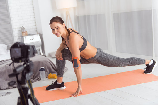 Happiness inside me. Pretty content athletic dark-haired young woman smiling and stretching while sitting on the carpet and making a video for her blog