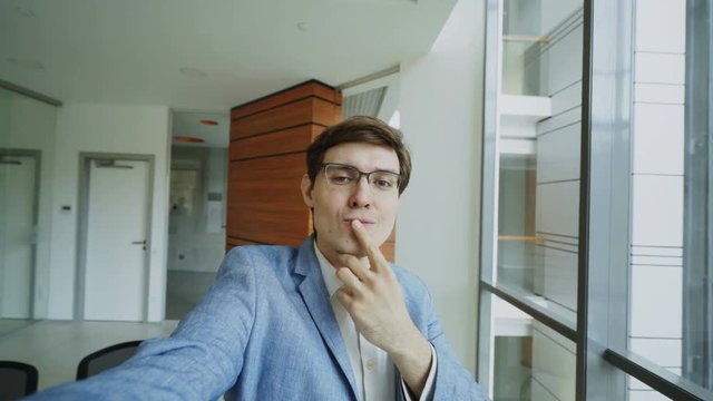 POV of young joyful businessman in glasses taking a selfie photo and have fun in modern office