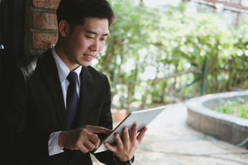 businessman in suit holding touchpad while standing outside building. young asian man using digital tablet for work outdoors