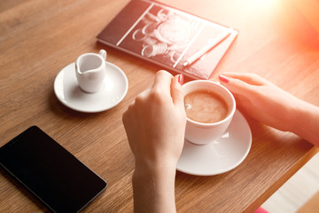 female hands with a black phone, close-up, background of a cup of coffee, table, notebook. Business lunch.
