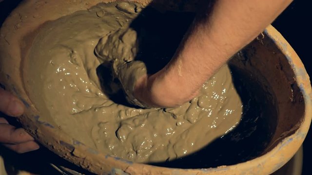 A close-up on a potters hand mixing wet clay. 