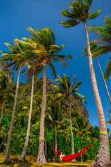 Fototapeta premium Woman relaxing in a hammock between palm trees on island, Palawan, Phillipines