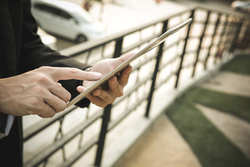 businessman in suit holding touchpad while standing outside building. young asian man using digital tablet for work outdoors