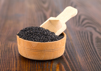 black sesame in a Cup and spoon on wooden surface.