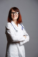 Photo of smiling female doctor in white lab coat and with phonendoscope in glasses