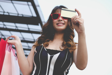 happy woman holding colorful shopping bag outdoors. shopaholic lady showing credit card. shopper enjoy buying. consumerism & payment concept