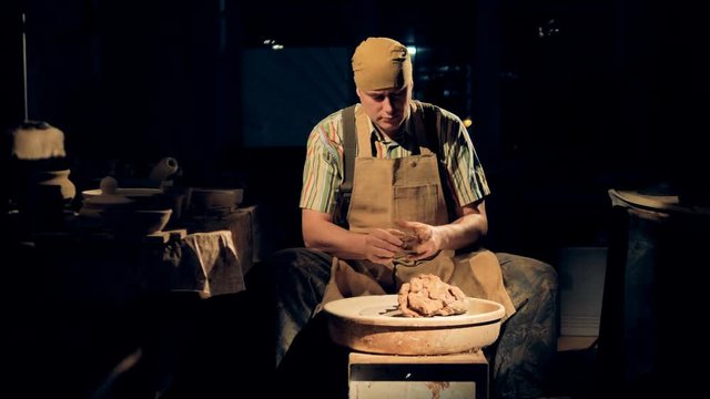 A potter in a dark room kneads clay.     