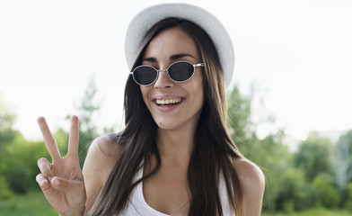 Portrait of a smiling beautiful young woman in a white hat and glasses looking at the camera with sign on Victory