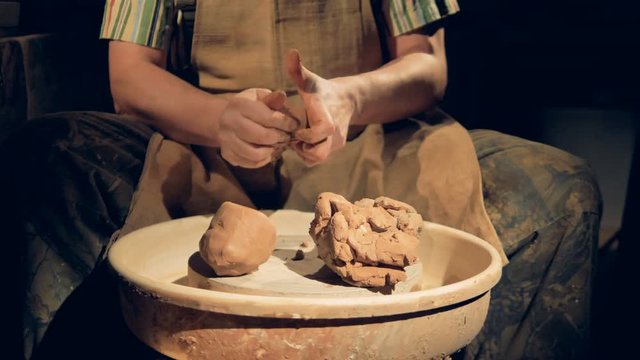 Potters hands work on several large lumps of crude clay. 