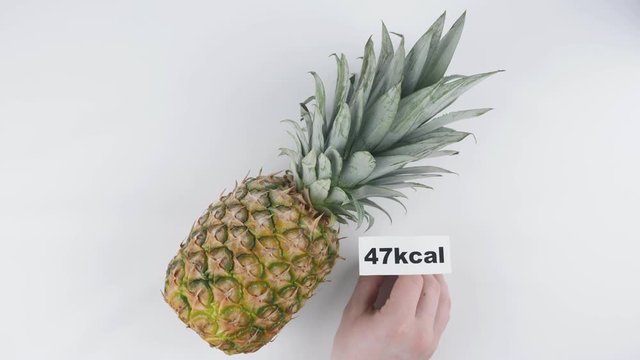 Amount of calories in pineapple, male hand puts a plate with the number of calories on a pineapple, top shot 60 fps