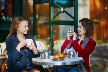 Two girls in cafe drinking coffee and using mobile phone in Paris, France