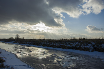 The sun behind the clouds above the frozen river