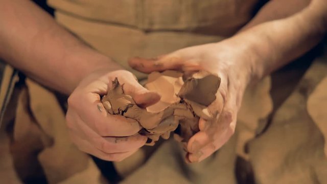 Potters fingers knead a medium lump of brown clay. 