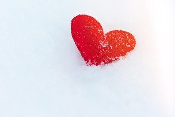 red felt heart figure on snow, winter day with sun glare