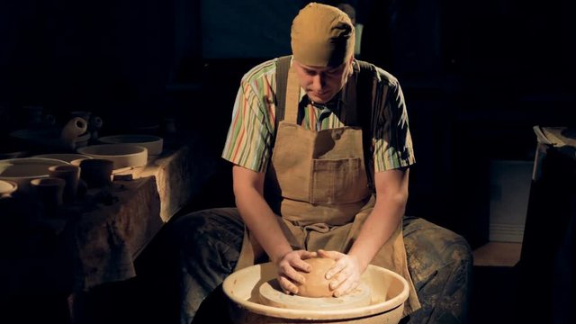 A potter presses a large clay ball onto a pottery wheel. 