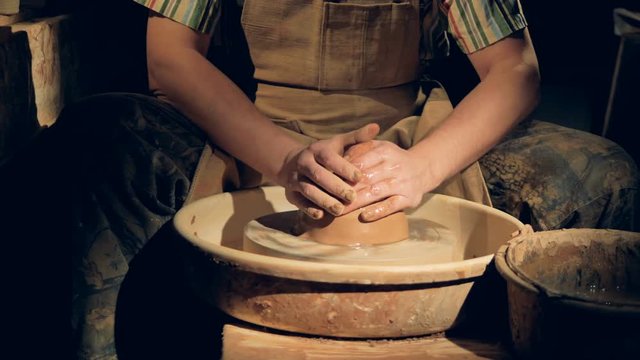 A potter wets a large lump of clay on a wheel. 