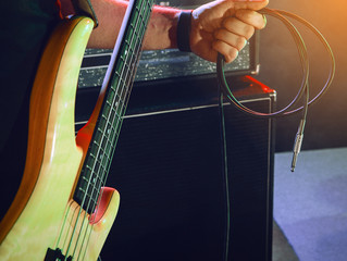 The bass guitarist connects the bass guitar to the amplifier on the stage.