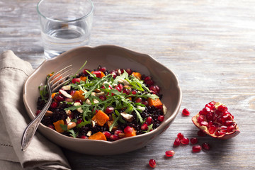 Salad with black rice, baked pumpkin, pomegranate seeds, arugula and nuts on a gray background. Delicious vegan food