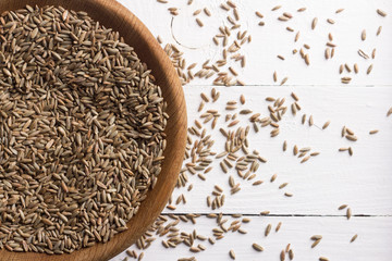 Seeds of rye for germination in a wooden bowl on a white background with free space