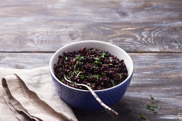 Black rice in a blue bowl on a wooden table, selective focus, rustic style. Simple healthy food