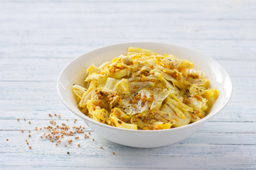 Pickled chinese cabbage with garlic and spices, mustard, turmeric, hot pepper in a white bowl on a blue background, selective focus. Healthy oriental food