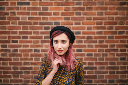 beautiful stylish girl with pink hair in hat posing at wall