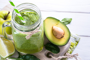 Green smoothie and ingredients on white wooden table.