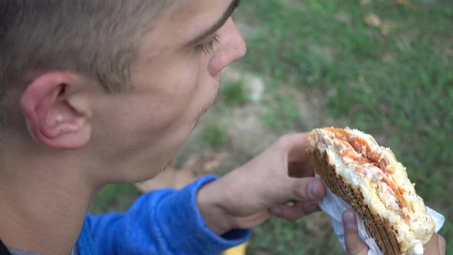 Young Man Teenager eating Doner Kebab at the City Park - Autumn Day