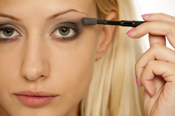 A young blonde woman applying eyeshadow with makeup brush