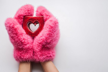From the bottom of my heart. Close up part of woman in mittens holding little red heart against white background