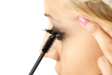 A young blonde woman applying mascara on her eyelashes