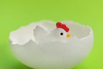 Little toy chicken in the eggshell on a green background