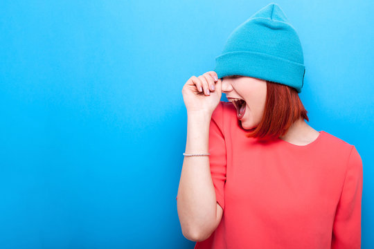 Happy cool hipster woman with her mouth open wearing a blue hat on blue background
