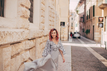 Fototapeta na wymiar smiling elegant girl in glamorous grey dress walking in Verona