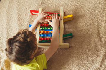 Preschooler baby learns to count. Cute child playing with abacus toy. Little boy having fun indoors at home, kindergarten or day care centre. Educational concept for preschool kids.