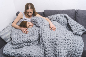 young lesbian couple relaxing under knitted wool blanket