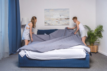 lesbian couple covering up bed in morning