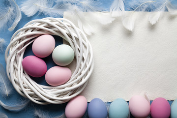 Easter eggs in the nest and white paper sheet on blue background