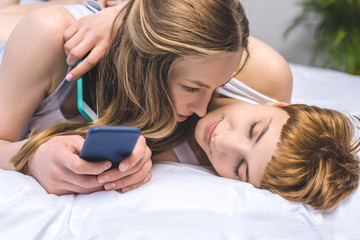 Obraz na płótnie Canvas young lesbian couple cuddling in bed while using smartphones