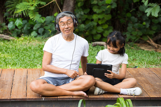Happy asian senior man Headphones Listening Music with grandchild in park